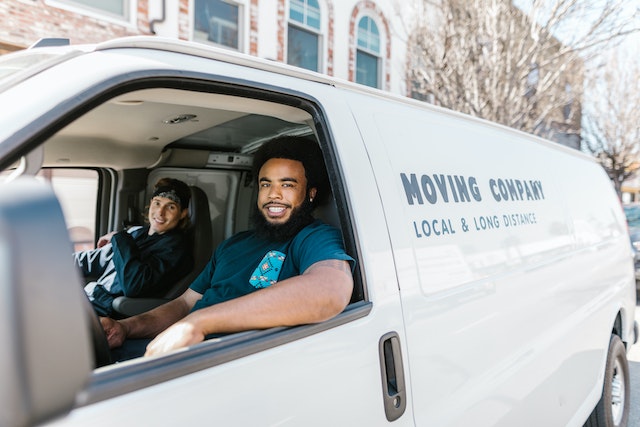 Two people inside a white moving van that reads “Moving Company, Local & Long Distance” on the side