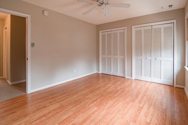 Clean empty room with brown wooden floors, gray walls, white closet doors, and a white ceiling fan