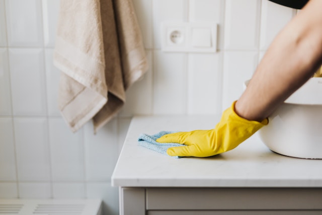 Hand in yellow rubber glove wiping down bathroom sink with a blue cloth