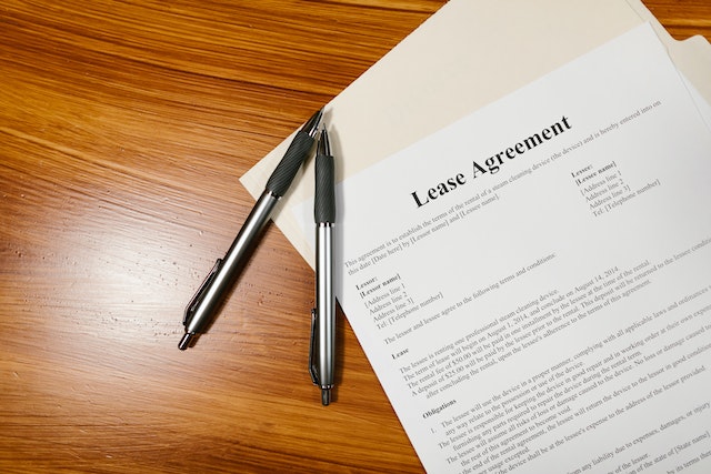 White paper with black text that reads “Lease Agreement” on a brown wooden table, next to two black ballpoint pens
