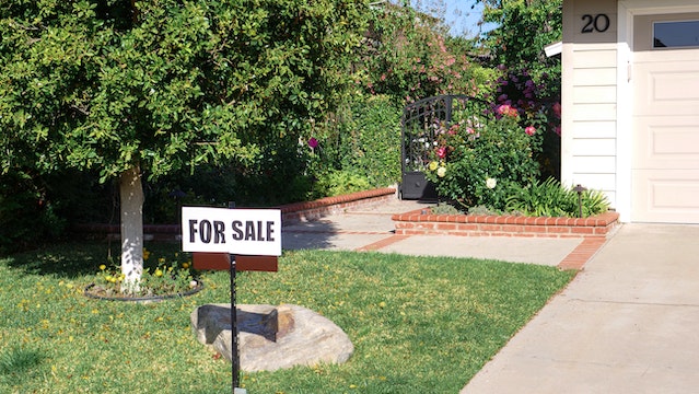 “For Sale” sign in a residential property’s green front lawn