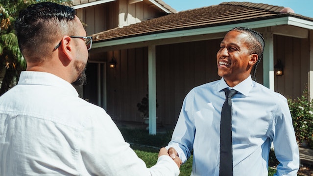 Two people in button-down shirts shaking hands in front of a residential property