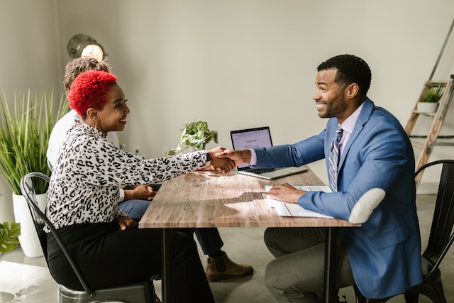 Two people sitting across each other at a table, shaking hands and smiling