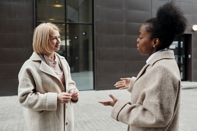 Two people wearing beige coats and business attire talking outside of a building