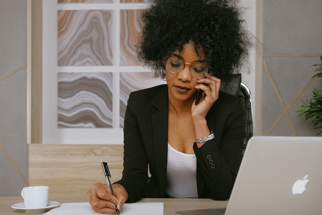 Person sitting at a desk with a laptop, taking notes and making a phone call