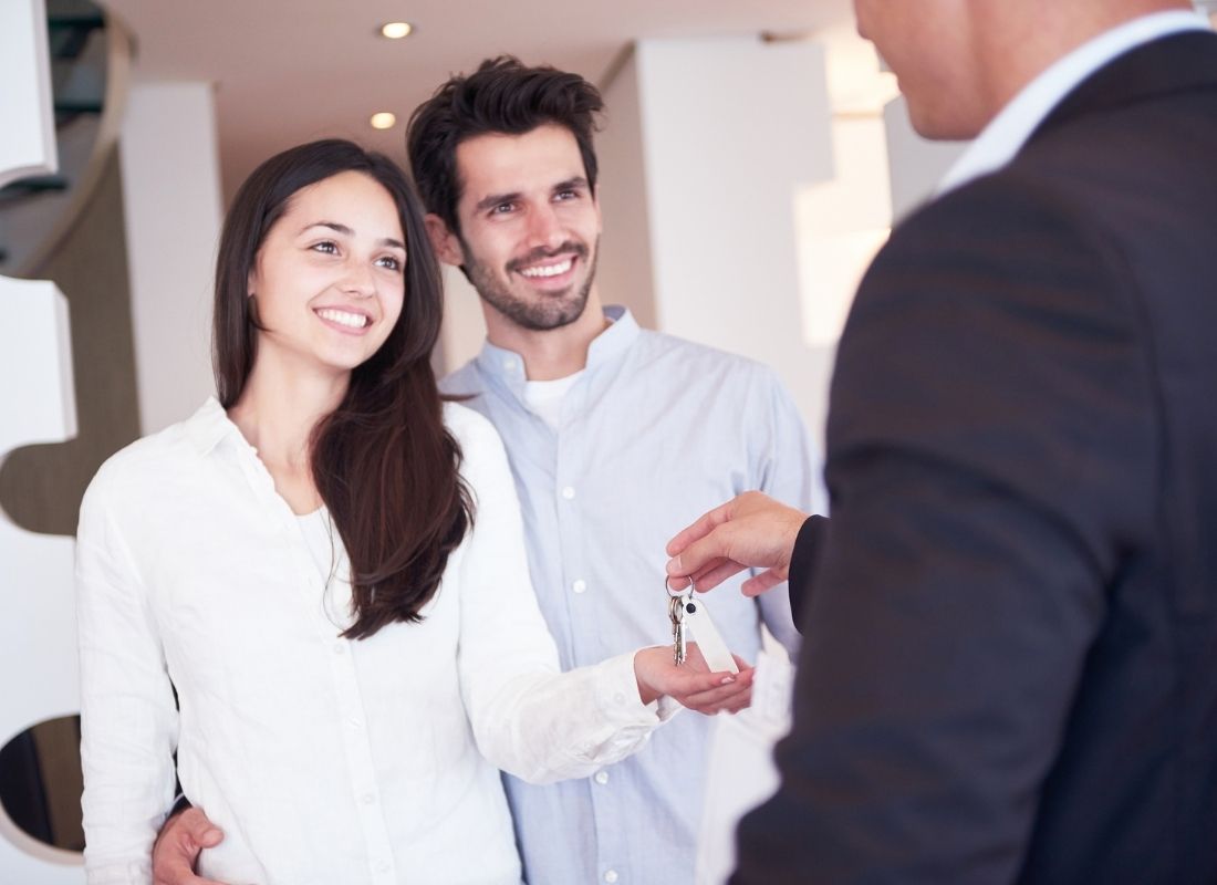 A person in a suit handing a set of keys to a smiling couple