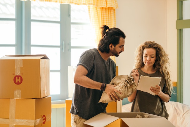 Two people in a room full of moving boxes, looking at a document