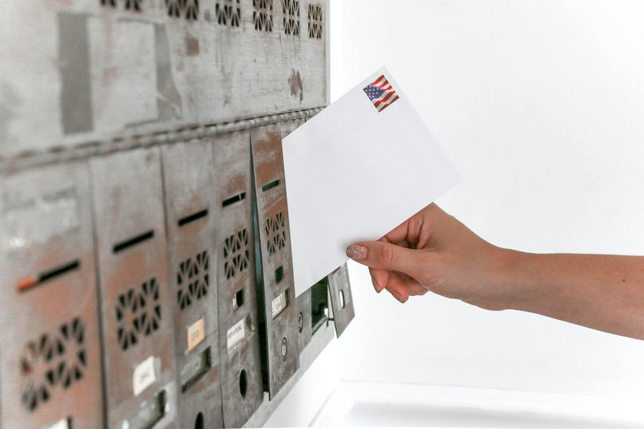 Hand slipping an envelope into a silver mailbox