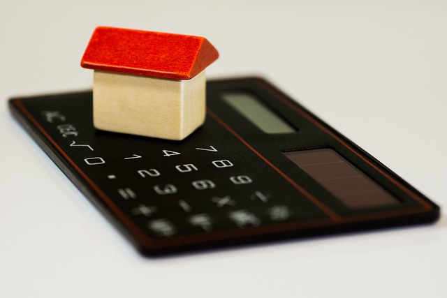 small-toy-house-made-of-wood-with-a-red-roof-sits-on-a-black-calculator-on-a-white-background