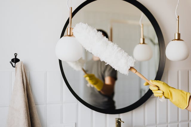 person-wearing-yellow-gloves-using-a-dusting-brush-to-clean-a-mirror