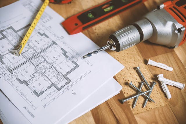 drill-screwdriver-ruler-screwdriver-and-other-tools-on-a-desk-with-papers-containing-a-floor-plan-on-it