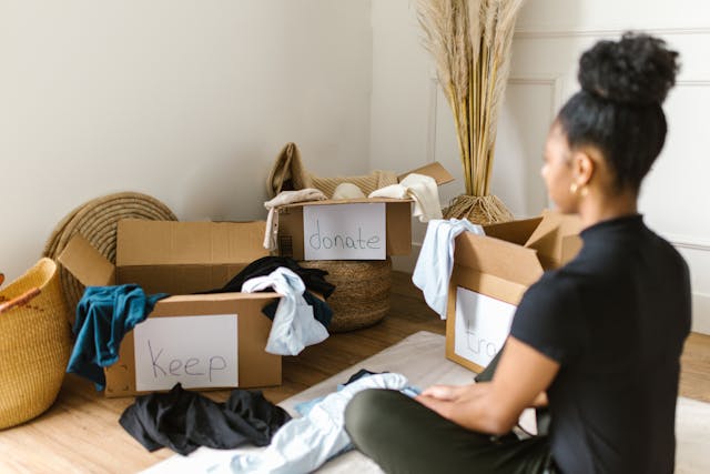 person-sitting-on-the-floor-with-three-boxes-of-clothes-labeled-keep-donate-trash