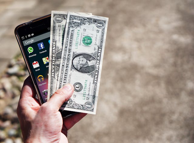 a-hand-holding-a-smartphone-and-two-one-dollar-bills