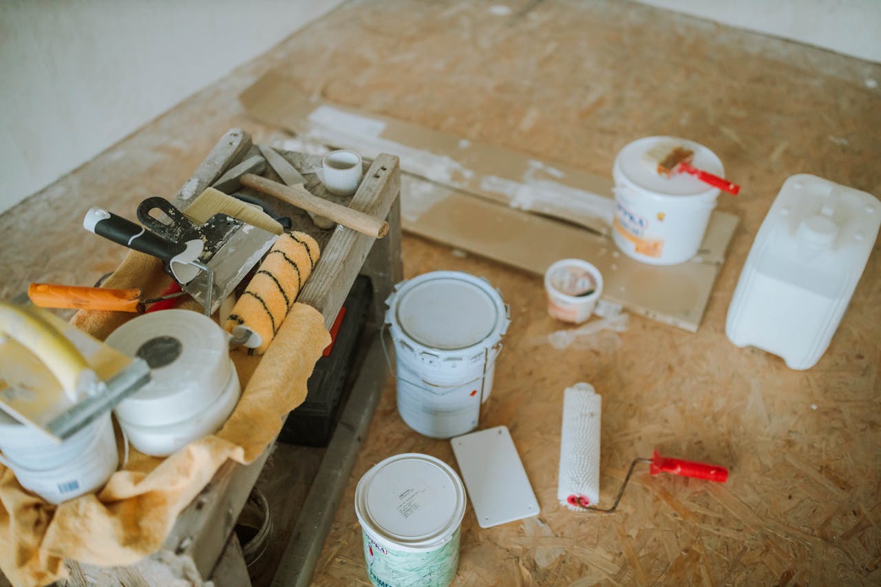 assorted-painting-and-renovation-supplies-on-a-wooden-surface-including-paint-rollers-brushes-buckets-and-cans