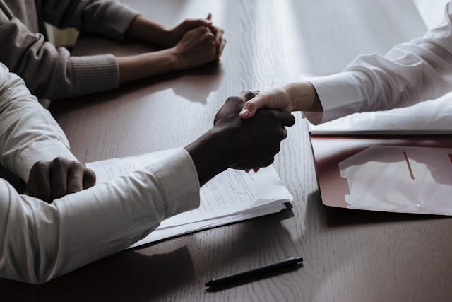 two-people-shaking-hands-over-a-contract-on-a-desk